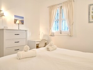 Ein Hotelzimmer mit Bett, Schreibtisch, Stuhl, Lampe und einem Vorhangfenster.