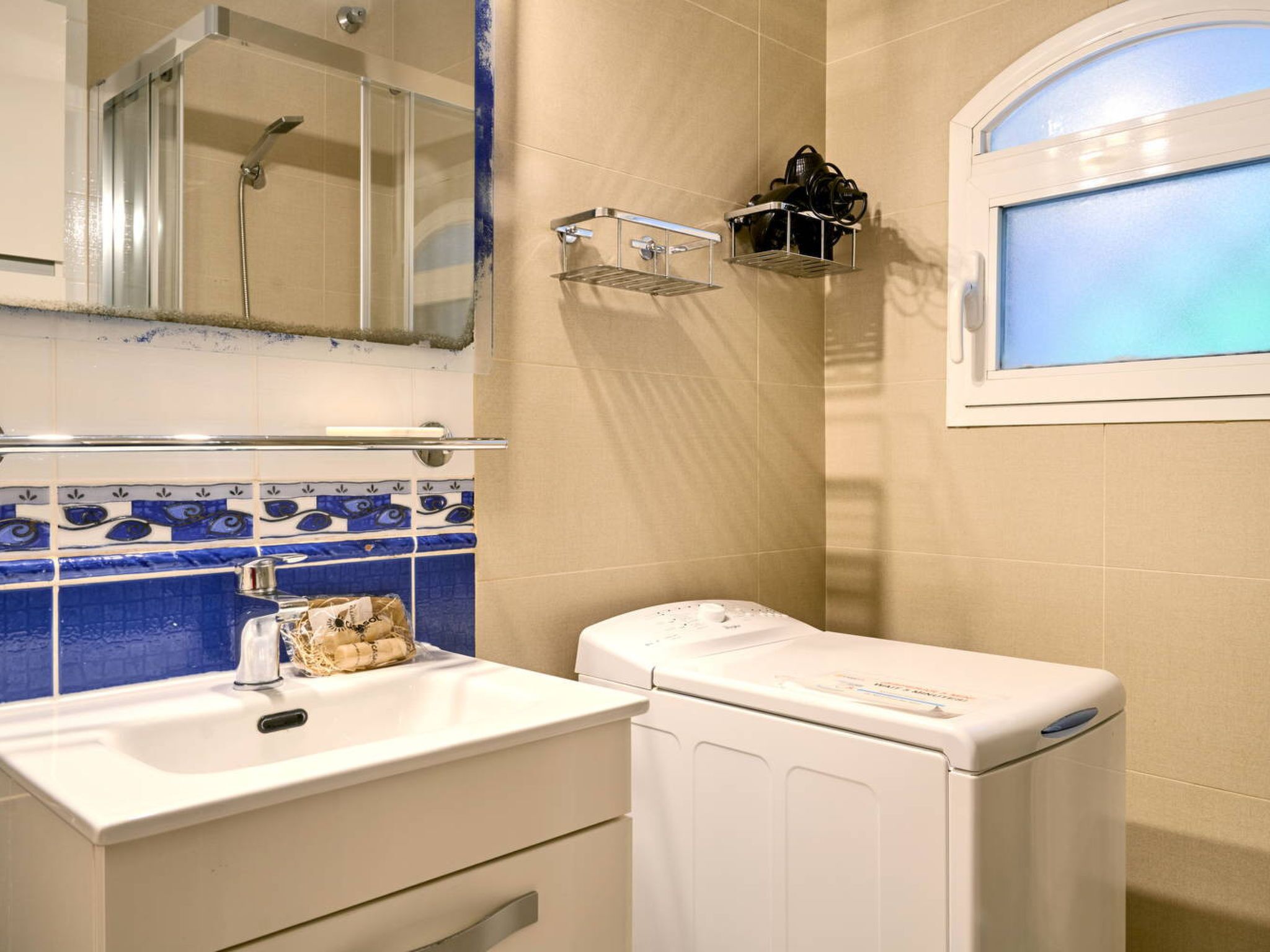 A bathroom with a white sink, a mirror, a towel rack, a window, and a washing machine.
