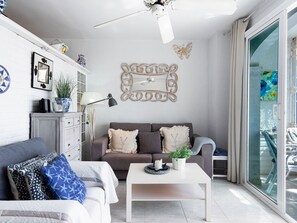 Ein modernes Wohnzimmer mit Deckenventilator, einem dekorativen Spiegel und einem grauen Sofa mit gemusterten Kissen.
