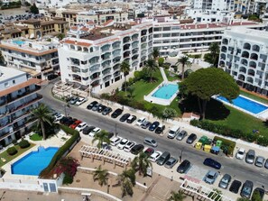 Ein mehrstöckiges Hotel mit Swimmingpool, Parkplatz und umgebender Bepflanzung.
