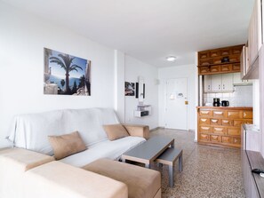 A living room with a sofa, a coffee table, and a kitchen area with wooden cabinets and a countertop. - Apartment  by Interhome (Nerja)