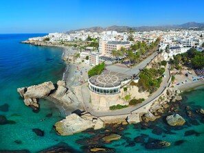 An aerial view of a coastal town with a prominent circular building with a star-shaped roof, surrounded by a rocky coastline and clear blue waters. - Apartment  by Interhome (Nerja)
