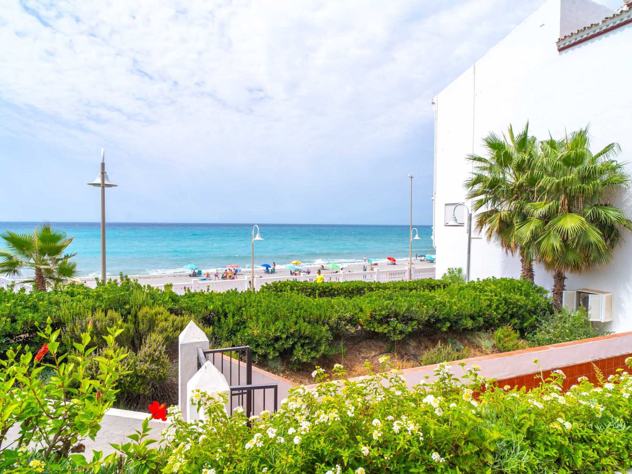 Eine Küstenansicht mit Strand, Palmen und einem weißen Gebäude mit Balkon mit Blick aufs Meer.