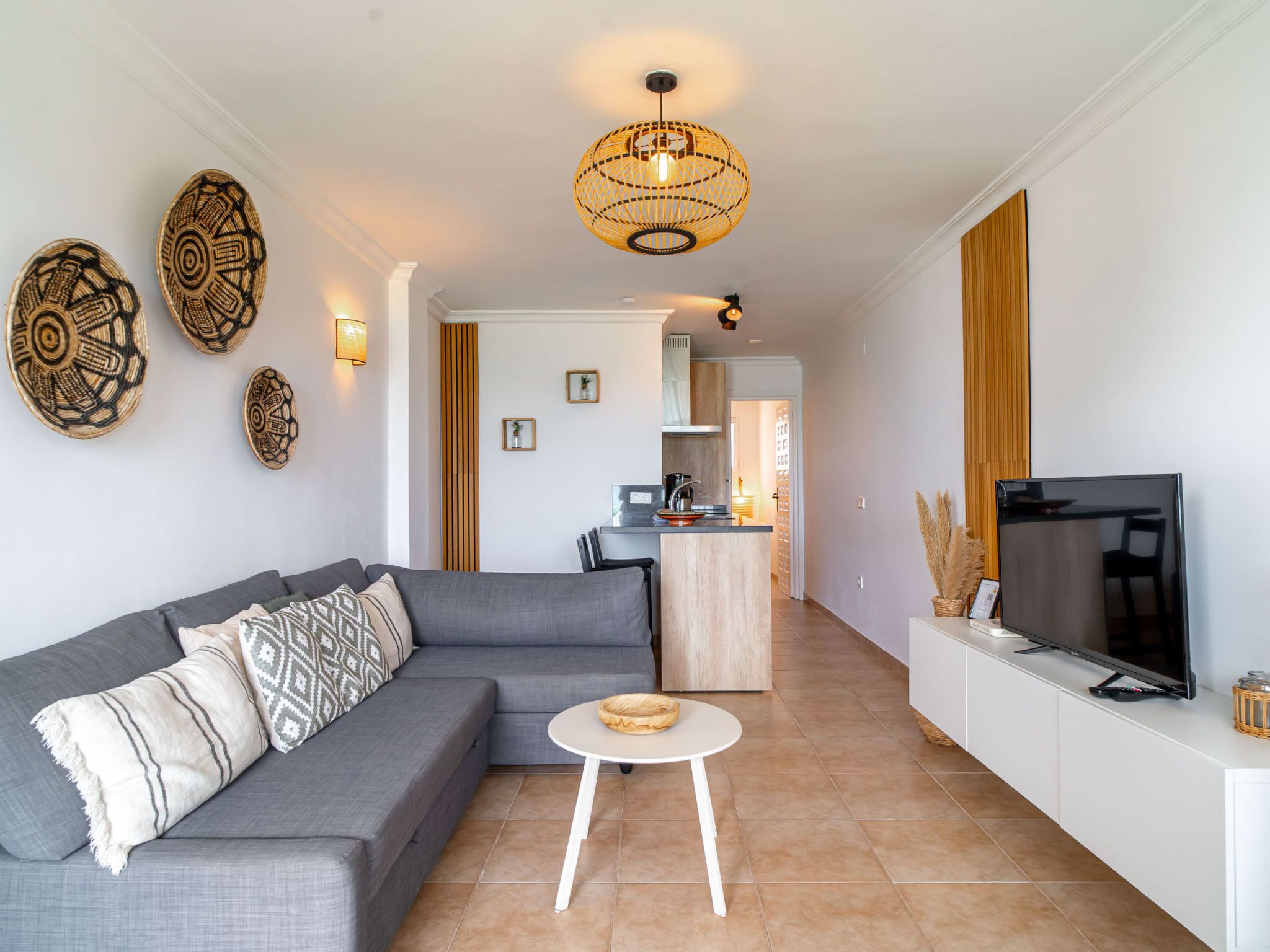 A modern living room with a grey sofa, a round coffee table, and a TV on a white cabinet.
