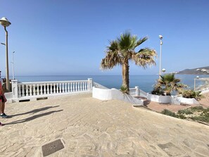Ein gepflasterter Weg mit weißer Brüstung, Palmen und Blick aufs Meer.