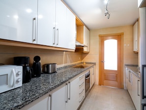 Una cocina moderna con gabinetes blancos, encimera de granito y electrodomésticos de acero inoxidable.
