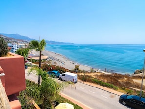 Una carretera costera con playa, vehículos y edificios al fondo.