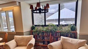 A room with two beige armchairs, a patterned carpet, a bookshelf, and a window with a view of snow-covered buildings.