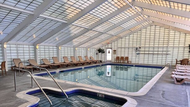 An indoor swimming pool with tiled walls, multiple lounge chairs, and a clear ceiling.