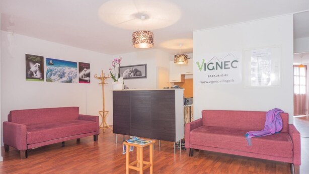 A modern living room with two sofas, a wooden coffee table, a reception desk, and wall-mounted artwork. - Residence Village Vignec (Vignec)