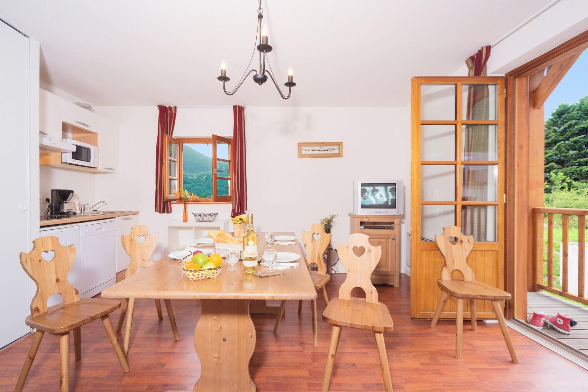 A dining area with a wooden table, chairs, a chandelier, a kitchen with a microwave, and a TV.