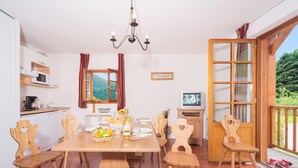 A dining area with a wooden table, chairs, a chandelier, a kitchen with a microwave, and a TV. - Residence Village Vignec (Vignec)
