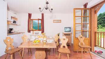 A dining area with a wooden table, chairs, a chandelier, a kitchen with a microwave, and a TV.