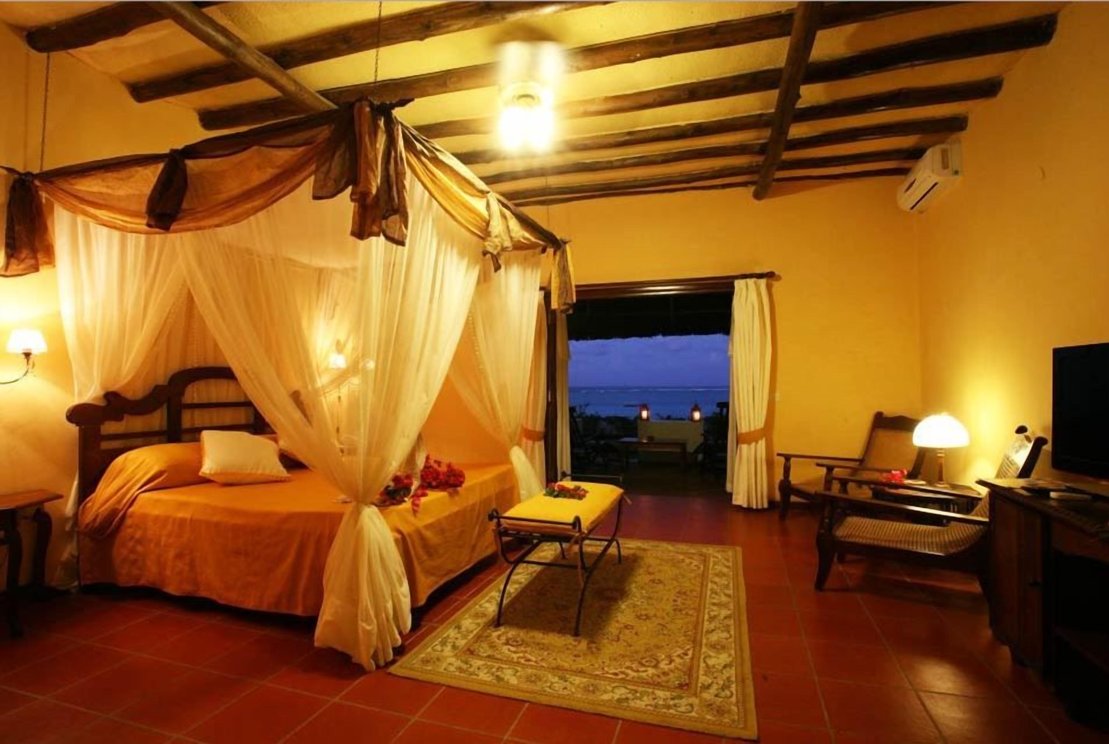 A bedroom with a bed, a chair, a table, and a view of the outdoors.