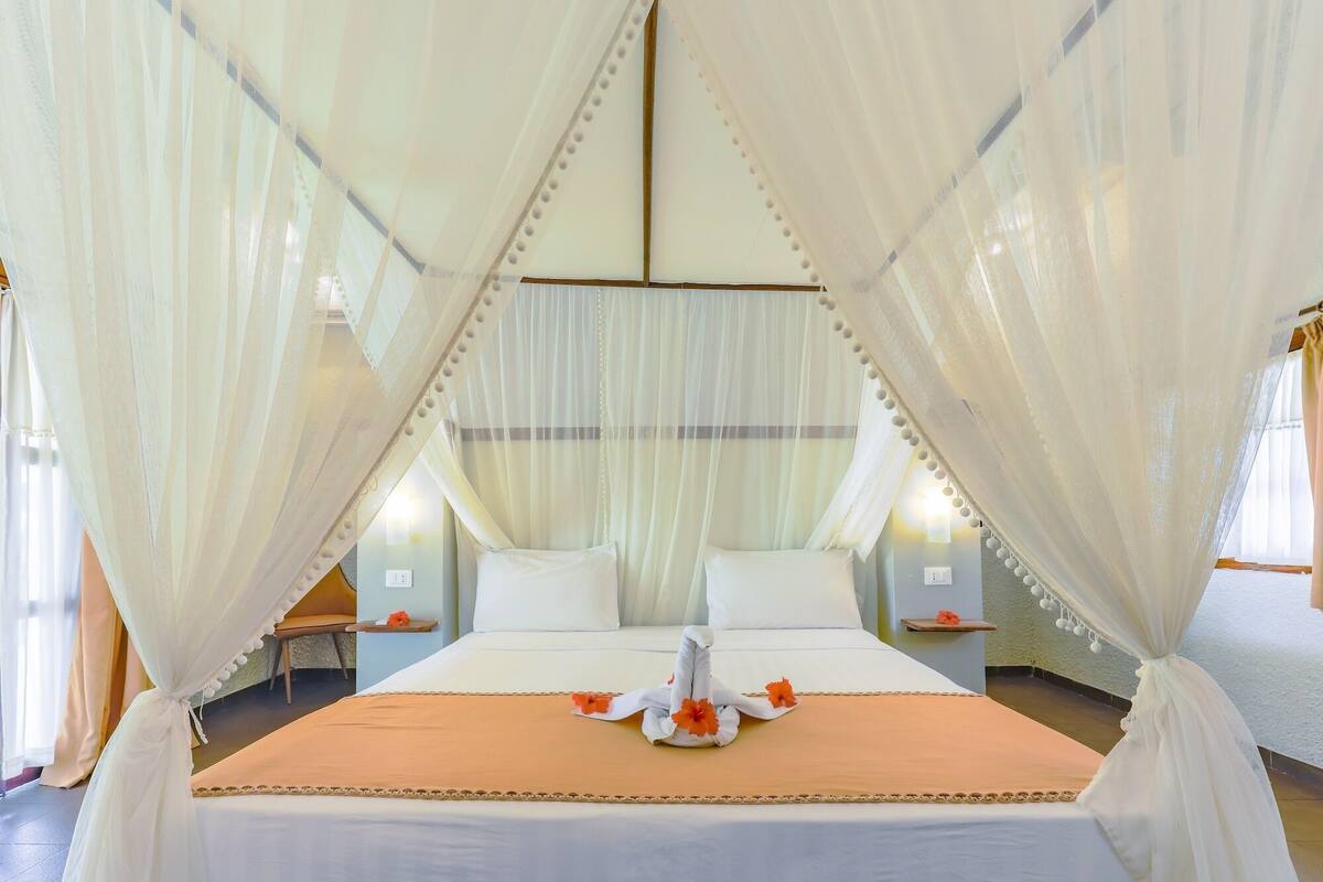 A hotel room with a bed, white curtains, and a decorative towel on the bed.