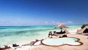 A wooden deck with a heart-shaped pool, thatched umbrellas, and a view of the ocean. - Karafuu Hotel Beach Resort (Michamvi)