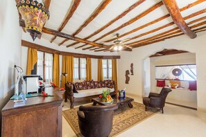 Una habitación con techo de madera, un sofá, una mesa de centro con fruta, una silla y un escritorio con lámpara.