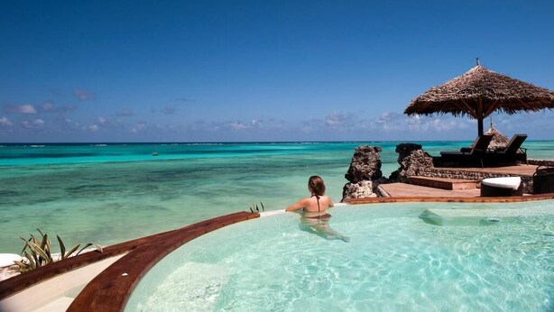 A clear blue sea, a woman in a pool, and a thatched umbrella. - Karafuu Hotel Beach Resort (Michamvi)