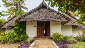 A traditional thatched-roof house with a white exterior, a wooden door, and steps leading to the entrance. - Karafuu Hotel Beach Resort (Michamvi)