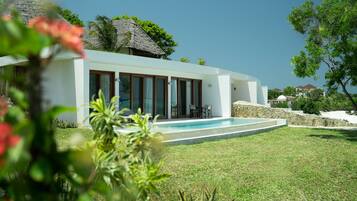 A modern house with a swimming pool, surrounded by a well-maintained lawn and tropical vegetation.