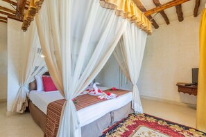 Habitación con cama bajo dosel, cabecera de madera, mesita de noche y alfombra estampada.