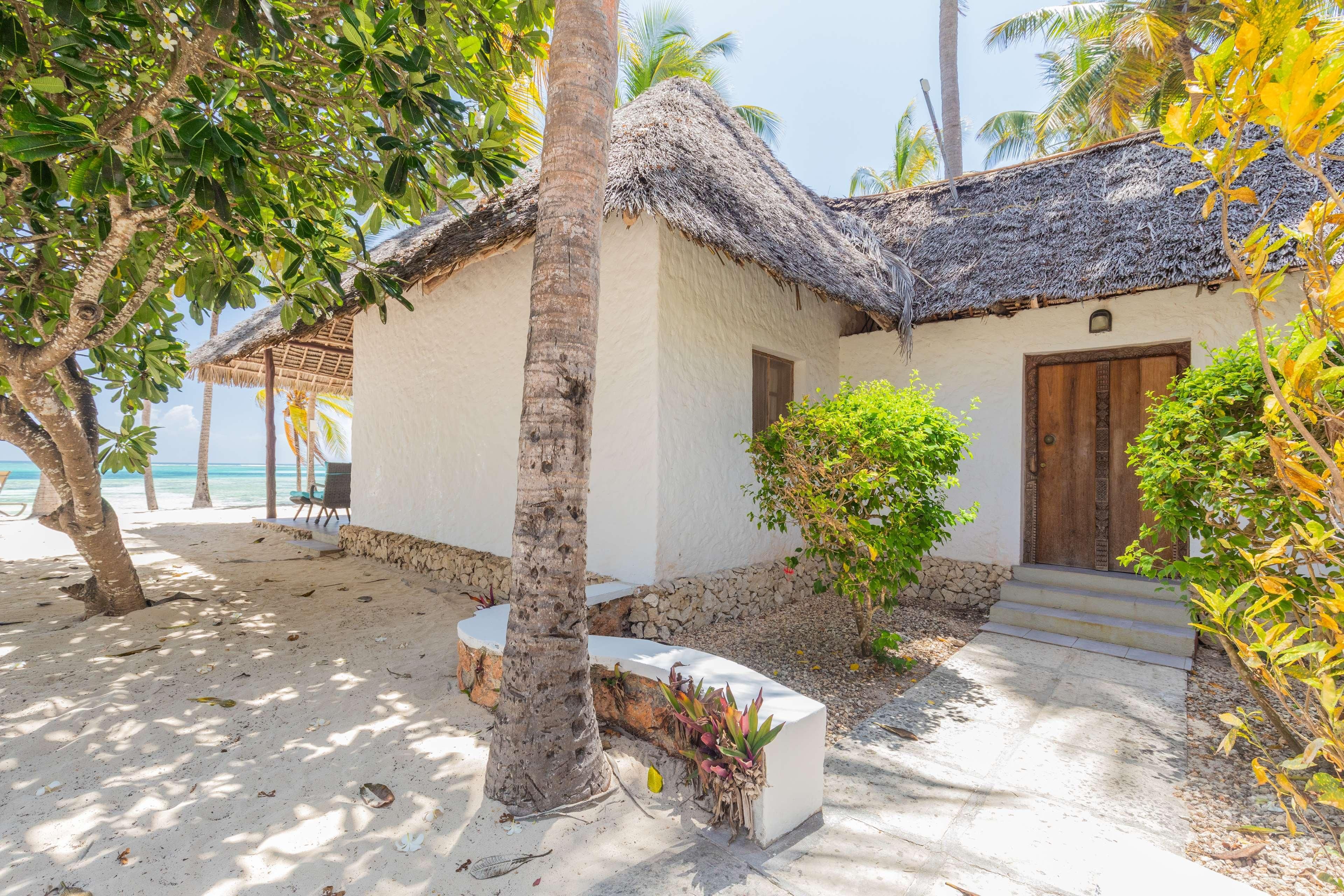 A beachside hut with a thatched roof, a wooden door, and a small garden area.