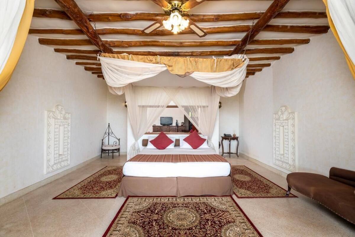 A bedroom with a canopy bed, a ceiling fan, and a large rug.
