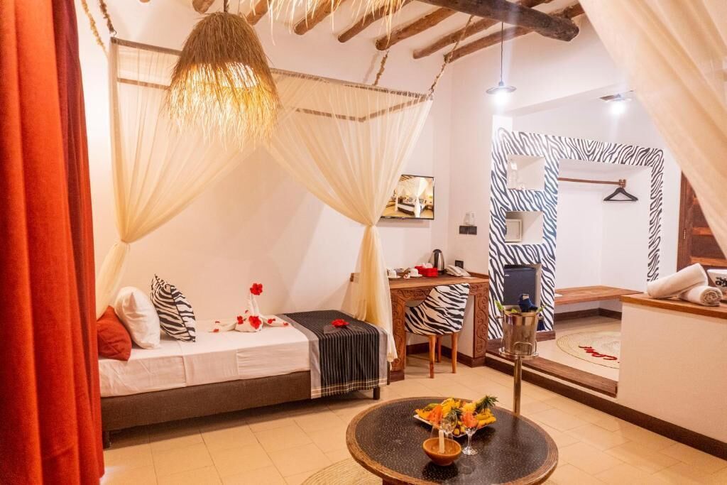 A bedroom with a bed, a desk, a chair, a round table with a vase, and a zebra-patterned wall.