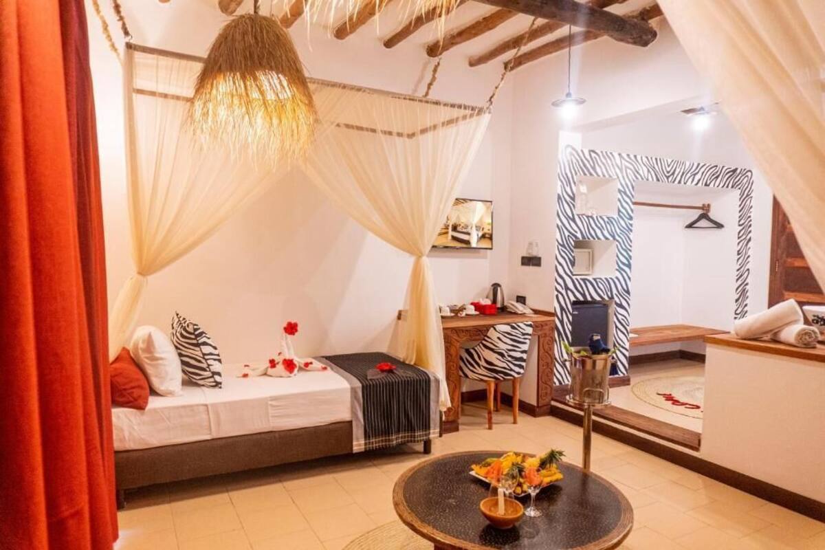 A bedroom with a bed, a desk, a chair, a round table with a vase, and a zebra-patterned wall.