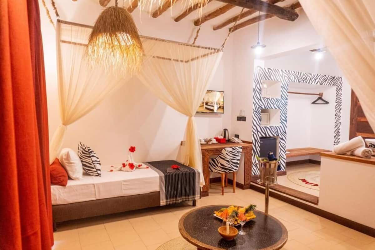 A bedroom with a bed, a desk, a chair, a round table with a vase, and a zebra-patterned wall.