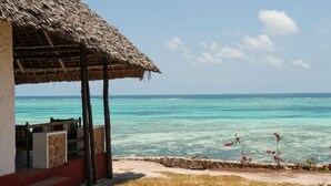 A beachside hut with a thatched roof, a stone wall, and a view of the ocean. - Karafuu Hotel Beach Resort (Michamvi)