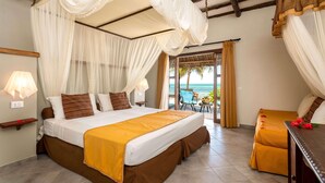 A bedroom with a bed, a bedside table, a chair, and a view of the ocean. - Karafuu Hotel Beach Resort (Michamvi)