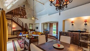 A spacious living area with a high ceiling, wooden staircase, and a dining table with chairs. - Karafuu Hotel Beach Resort (Michamvi)
