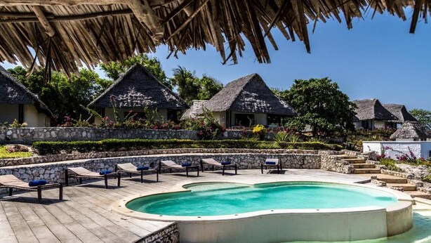 A resort with a swimming pool, lounge chairs, and thatched-roof villas. - Karafuu Hotel Beach Resort (Michamvi)