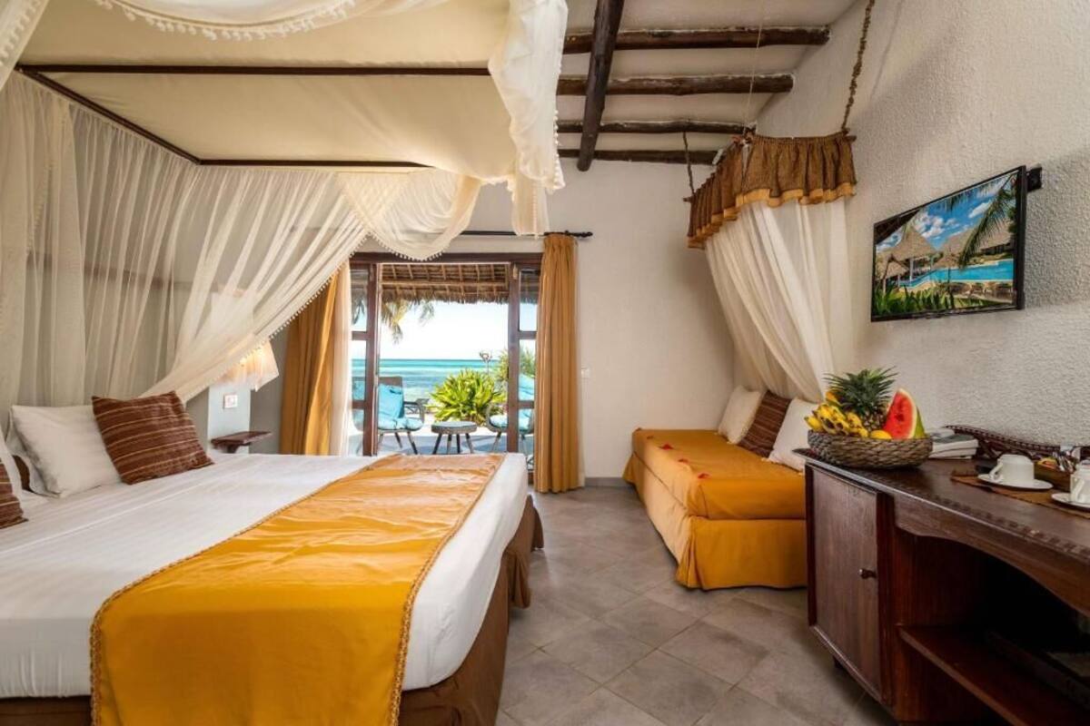 A hotel room with a bed, a sofa, a desk with a fruit bowl, and a painting on the wall.