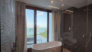 A modern bathroom with a freestanding bathtub, a glass-enclosed shower, and a large window offering a view of the outdoors. - Karafuu Hotel Beach Resort (Michamvi)