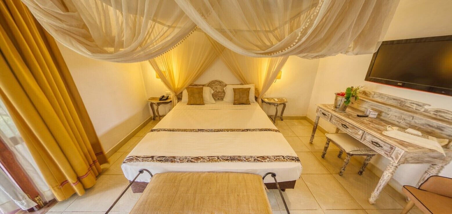 A bedroom with a large bed, a TV, a desk, and a chair.