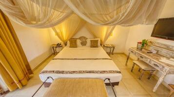 Quarto com uma cama grande, televisão, penteadeira com espelho e escrivaninha.