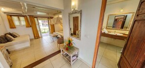 A hotel room with a bed, a sitting area with a sofa, a small table with a vase of flowers, a mirror, and a bathroom with a sink and mirror. - Karafuu Hotel Beach Resort (Michamvi)