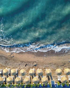 A beach with rows of sun umbrellas and lounge chairs, a sandy shore, and waves crashing onto the beach. - Catamaran Resort Hotel (Kemer)