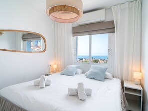 A hotel room with a large bed, two bedside lamps, a window with a view of the sea, and a mirror on the wall. - Casa Lovisa Private Pool by Casasol by Interhome (Nerja)