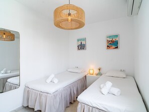 Ein Hotelzimmer mit zwei Einzelbetten, einer hängenden Korbschwinge-Lampe, einem Spiegel und zwei Wandbildern.