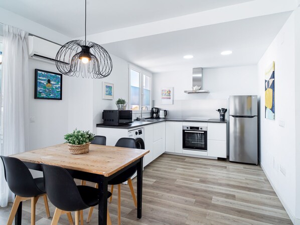 Une cuisine moderne avec des meubles blancs, une table à manger en bois, des chaises noires et un luminaire suspendu.