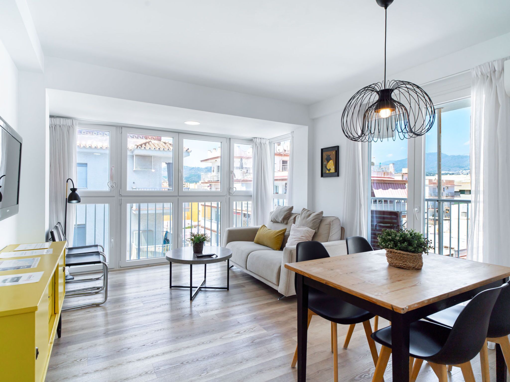 Ein modernes Wohnzimmer mit einer Couch, einem Esstisch, Stühlen und einem großen Fenster mit Blick auf Gebäude.