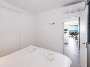 Ein modernes Hotelzimmer mit einem großen Bett, zwei aufgerollten Handtüchern, einer Dekoration mit Hirschgeweih und Blick aufs Meer durch eine Glastür.