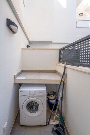 A compact laundry room with a front-loading washing machine, a small shelf, and a window with a black grid. - Terrazas de Ladera Duplex 1 by Casasol by Interhome (Nerja)