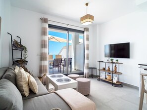 Ein modernes Wohnzimmer mit Sofa, Esstisch, Fernseher und einem Balkon mit Aussicht.