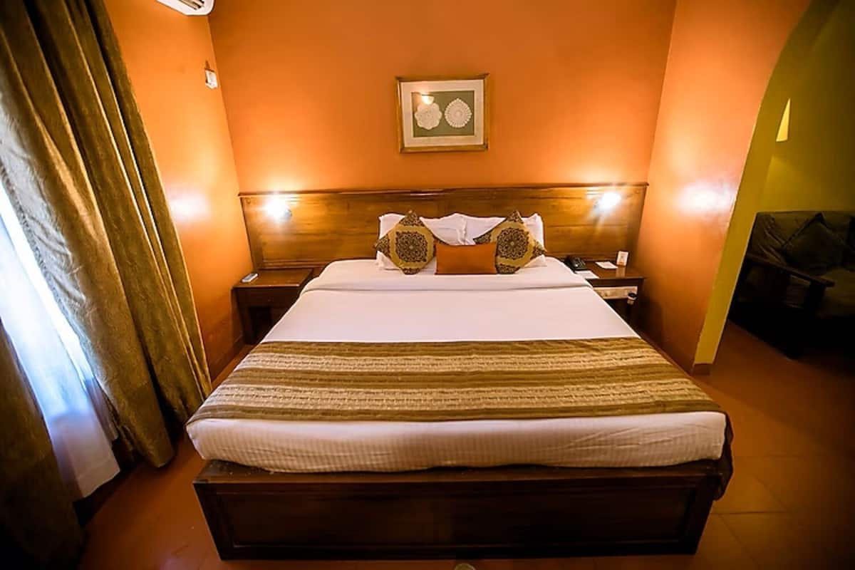 A hotel room with a large bed, a wooden headboard, a framed picture on the wall, and a curtain on the left side.