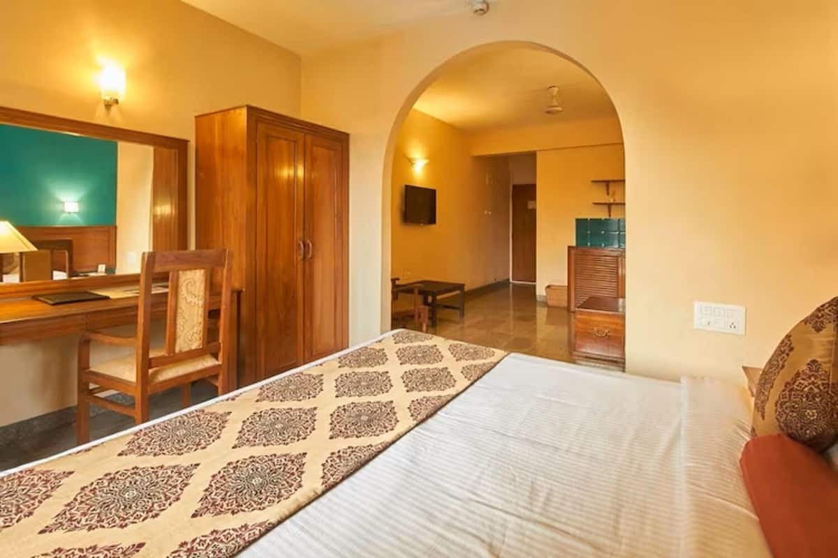 A hotel room with a bed, a desk, a chair, a wardrobe, and an arched doorway leading to another room.