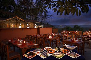 An outdoor dining area with tables set for meals, a chef preparing food, and a view of the landscape. - Pride Sun Village Resort (Arpora)